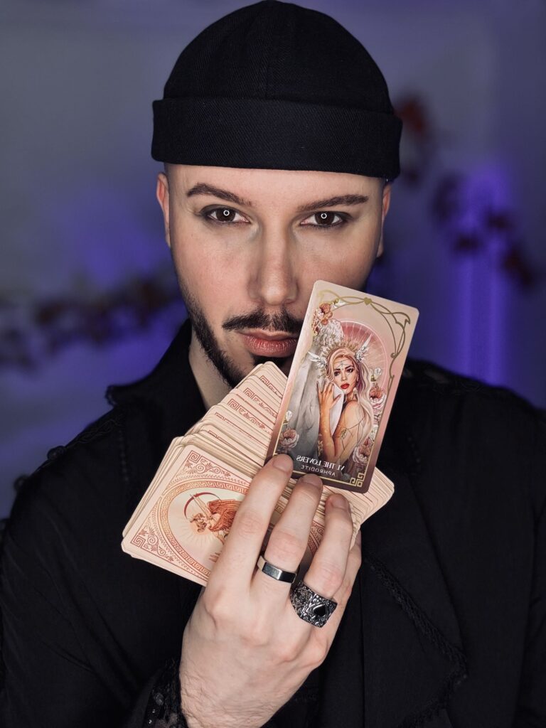 tarocista z ciemnym makijażem oczu w czarnej czapce trzymający w ręce karty tarota